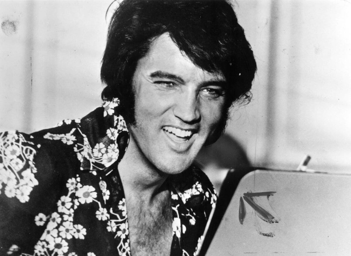 A black and white picture of Elvis wearing a floral shirt and laughing.