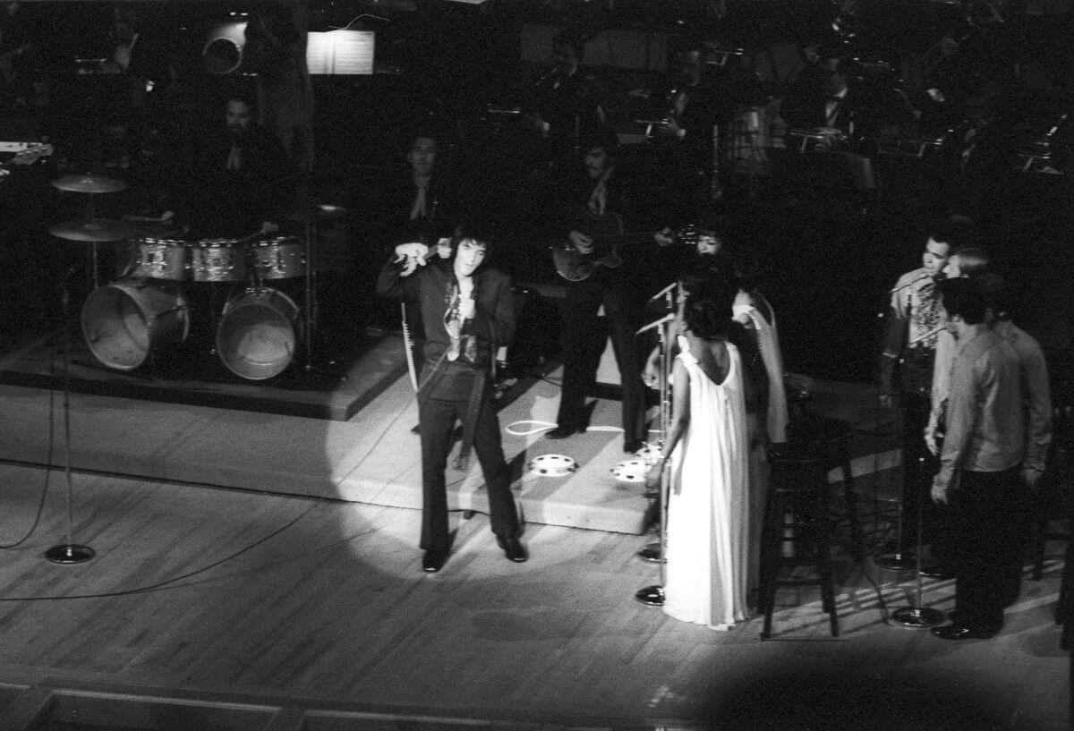 A black and white picture of Elvis Presley singing onstage with his backup singers. 