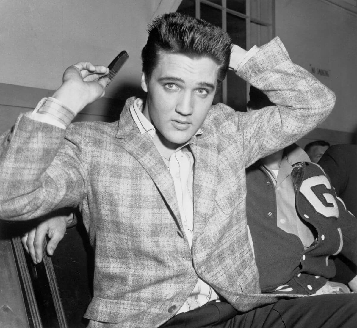 A black and white picture of Elvis Presley wearing a jacket and combing his hair.