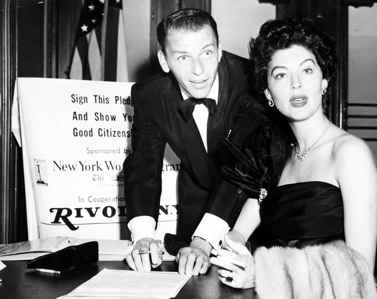 A black and white picture of Frank Sinatra and Ava Gardner holding pens while leaning over a stack of papers.