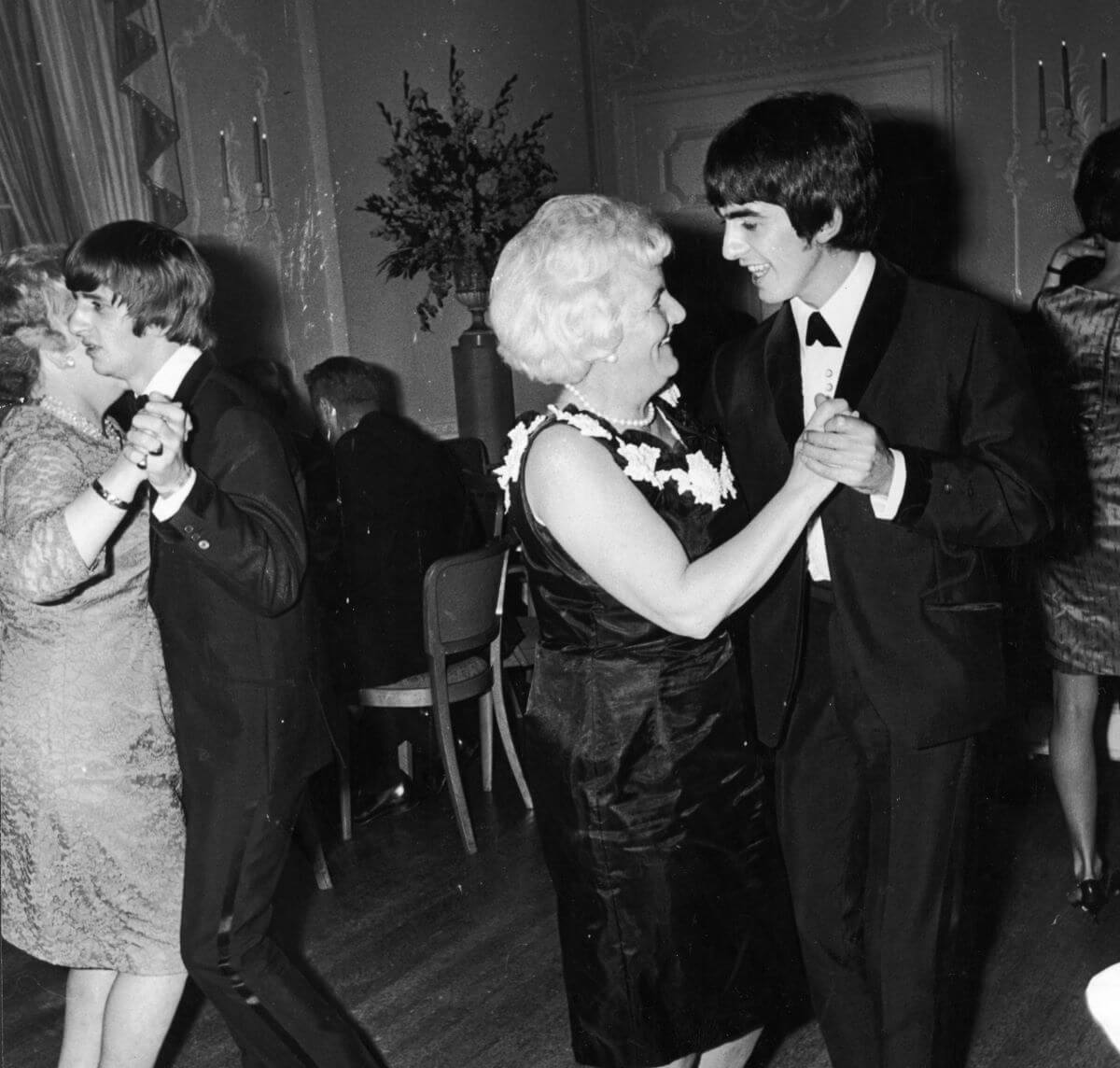 A black and white picture of George Harrison and his mom Louise Harrison dancing together. Ringo Starr and his mother dance behind them.