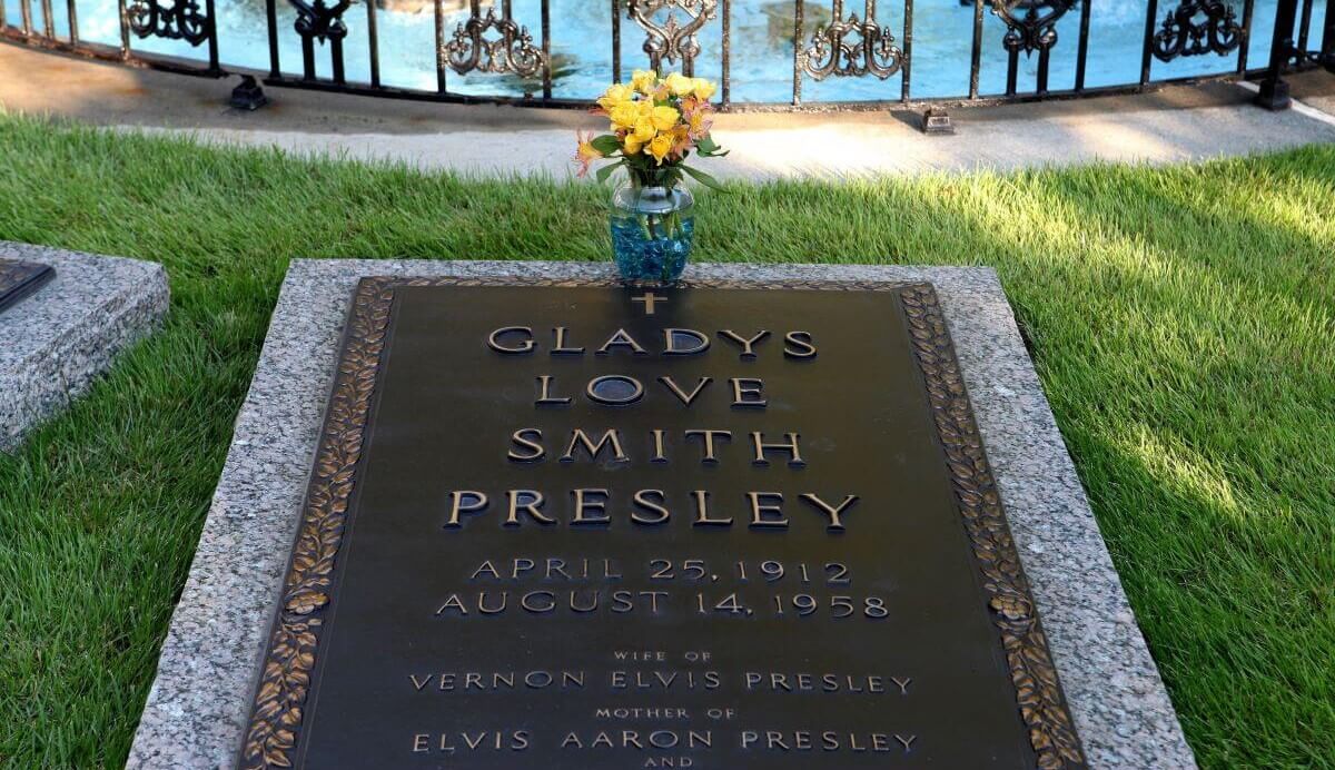 The gravestone for Gladys Love Smith Presley has a vase of yellow roses on top.
