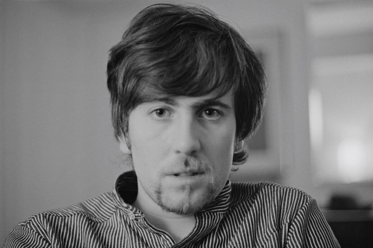 A black and white picture of Graham Nash wearing a stripped button-down shirt.