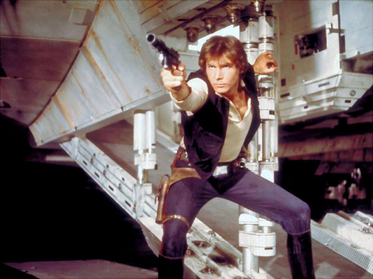 Harrison Ford crouches and holds up a gun as Hans Solo in 'Star Wars.'