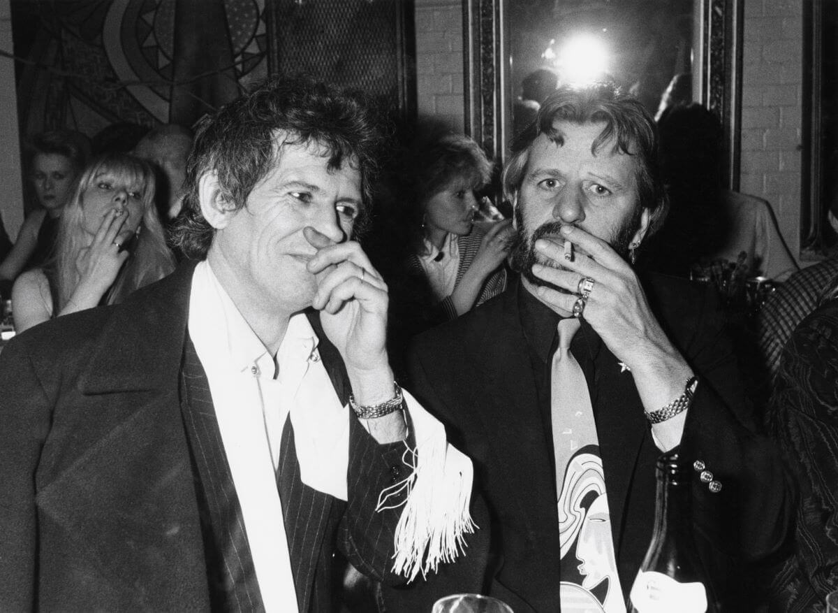 A black and white picture of Keith Richards standing next to The Beatles' Ringo Starr, who smokes a cigarette.