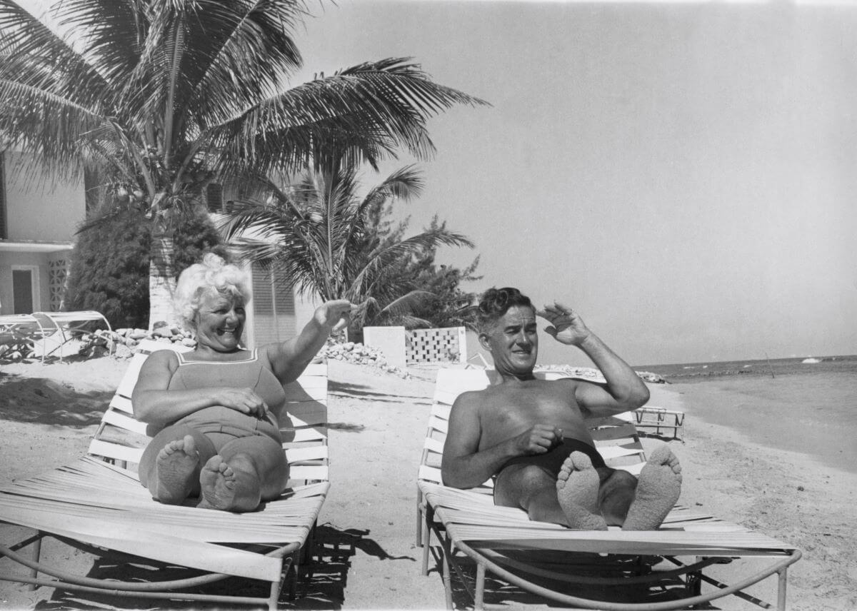 A black and white picture of Louise and Harold Harrison laying in lounge chairs on the beach.