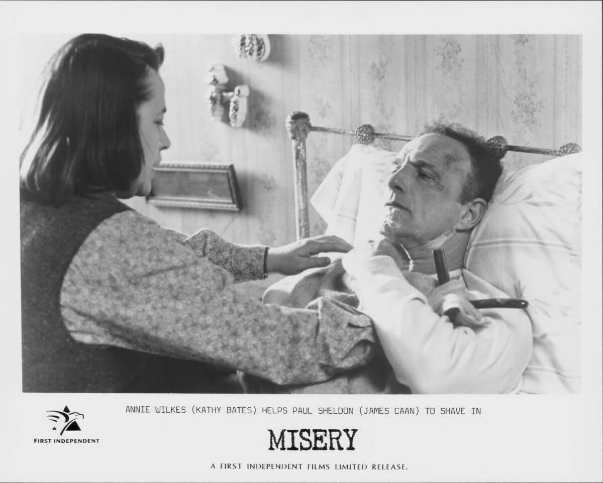 A poster for "Misery" that shows James Caan lying in bed while Kathy Bates shaves his face.