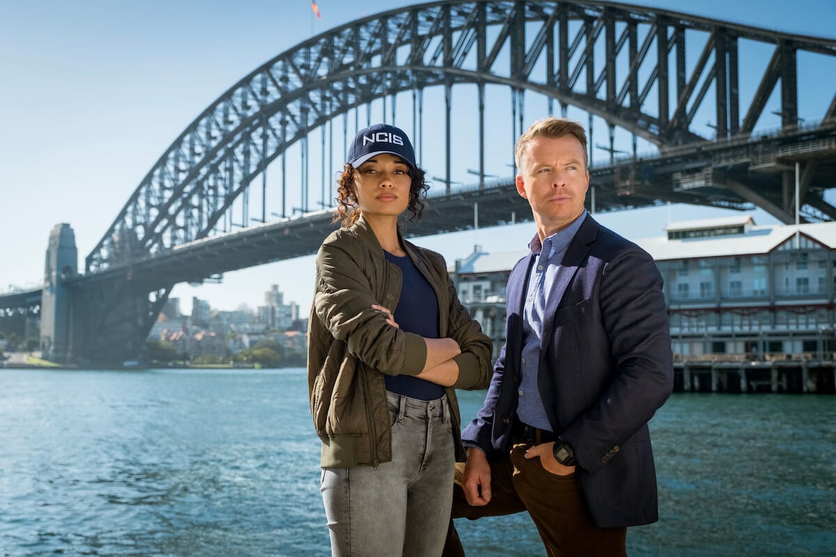 Olivia Swann and Todd Lasance of 'NCIS: Sydney' standing in front of a bridge