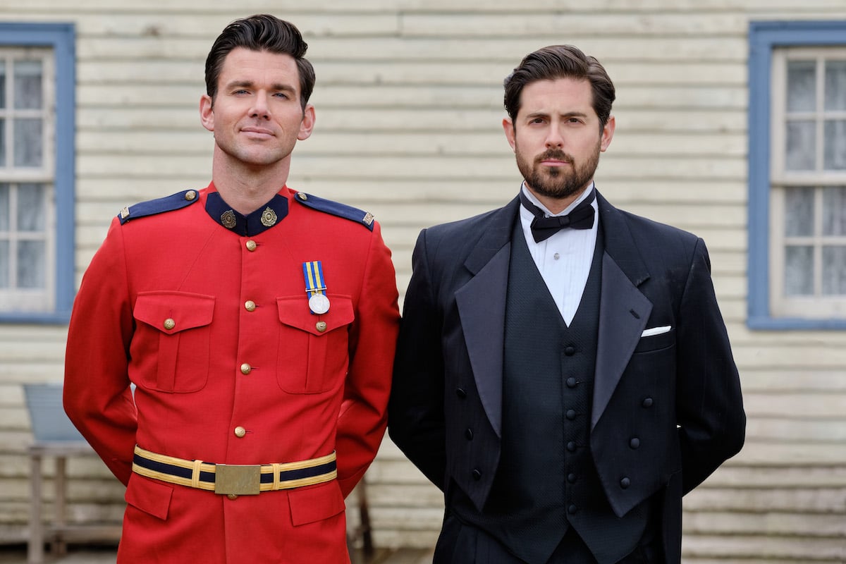 Nathan, in red mountie uniform, and Lucas, in a suit, standing next to each other in 'When Calls the Heart'