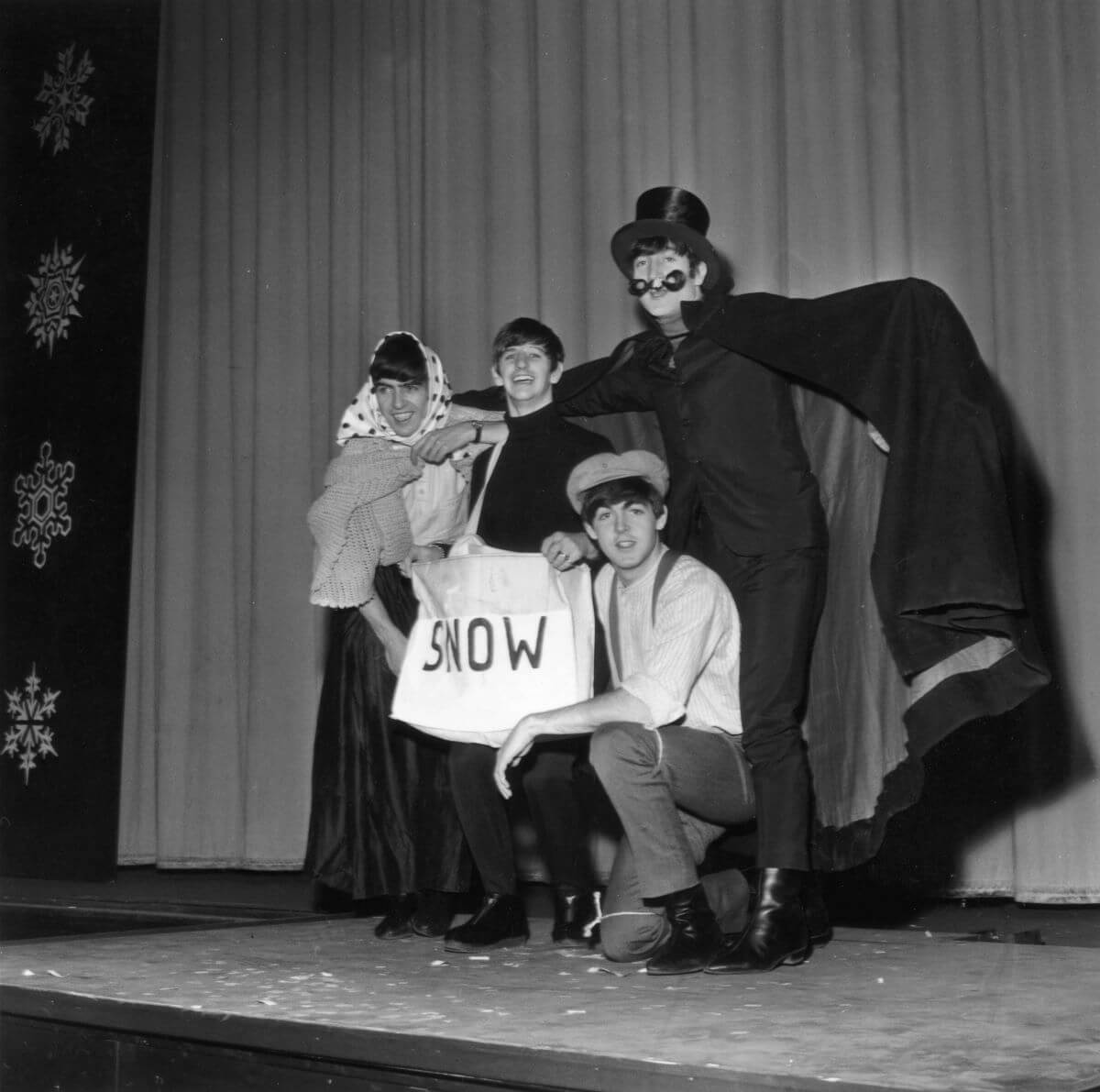 A black and white picture of The Beatles standing on a stage in costumes holding a sign that says "SNOW."