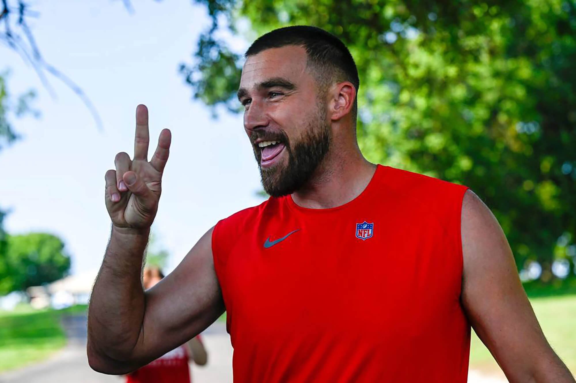 Taylor Swift's rumored boyfriend Travis Kelce from the Kansas City Chiefs wearing a red sleeveless shirt with his hand in a peace sign