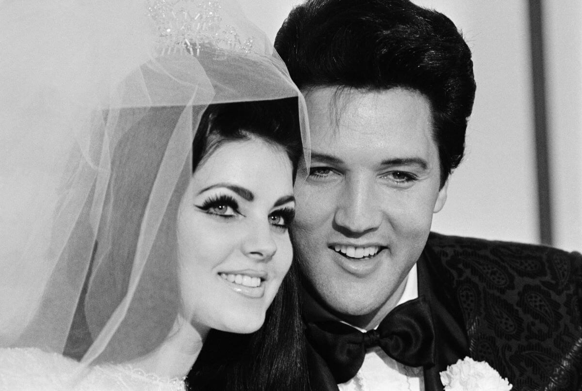 A black and white picture of Priscilla and Elvis Presley on their wedding day. She wears a veil and he wears a bow tie.