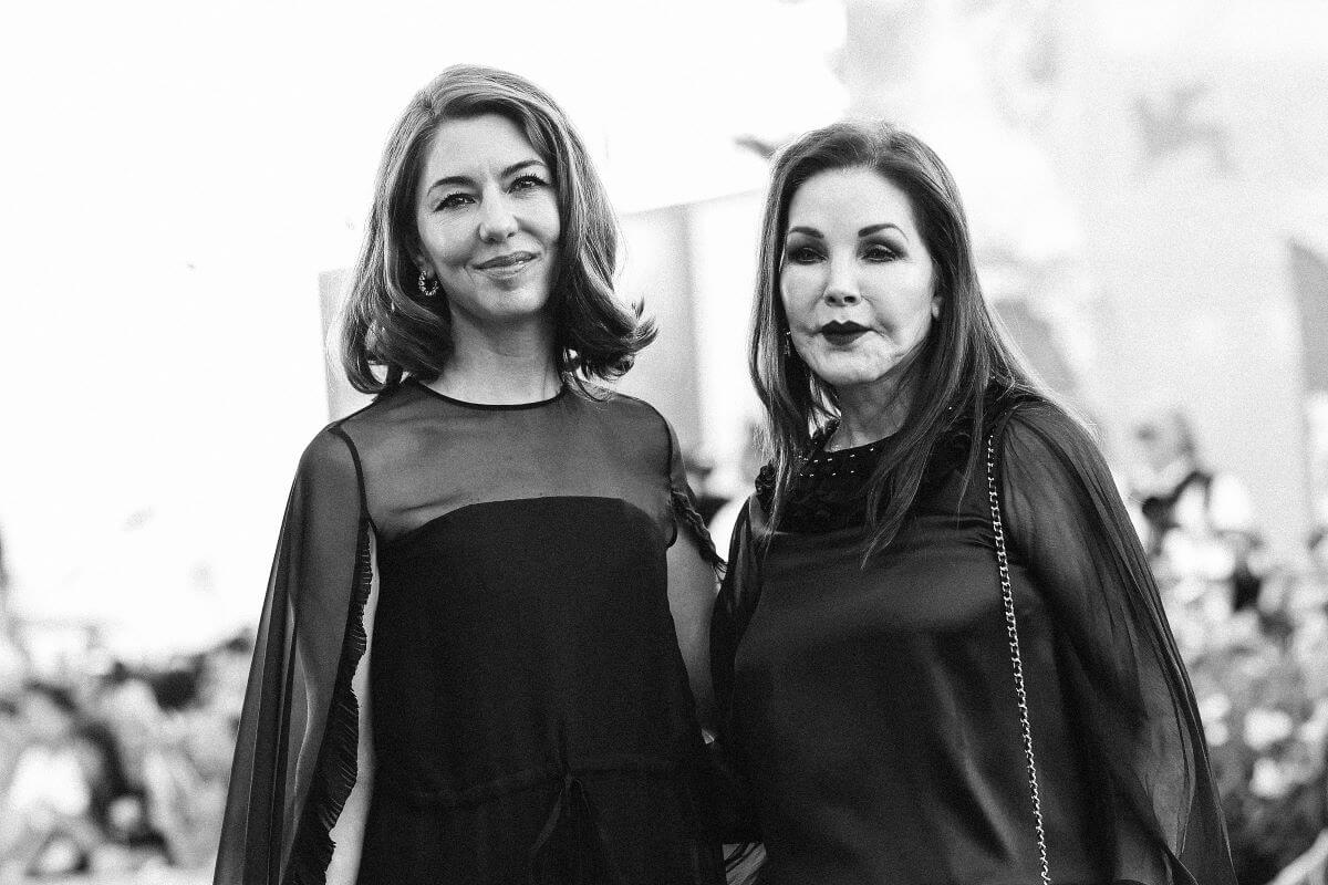 A black and white picture of Sofia Coppola and Priscilla Presley wearing dresses and standing together.