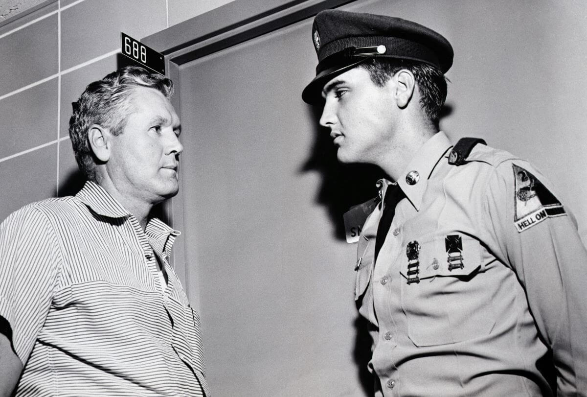 A black and white picture of Elvis and his father Vernon looking at each other. Elvis wears his military uniform.