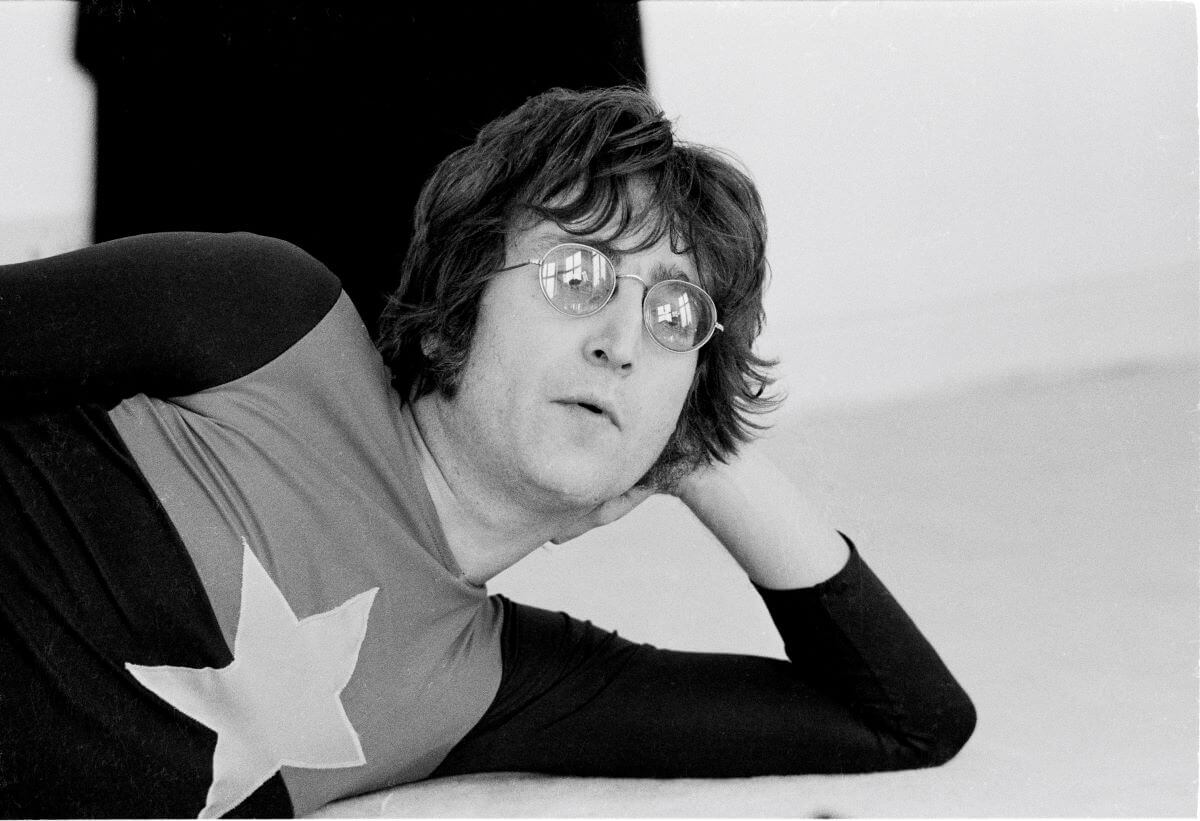 A black and white picture of John Lennon laying on his side and resting his head in his hand.