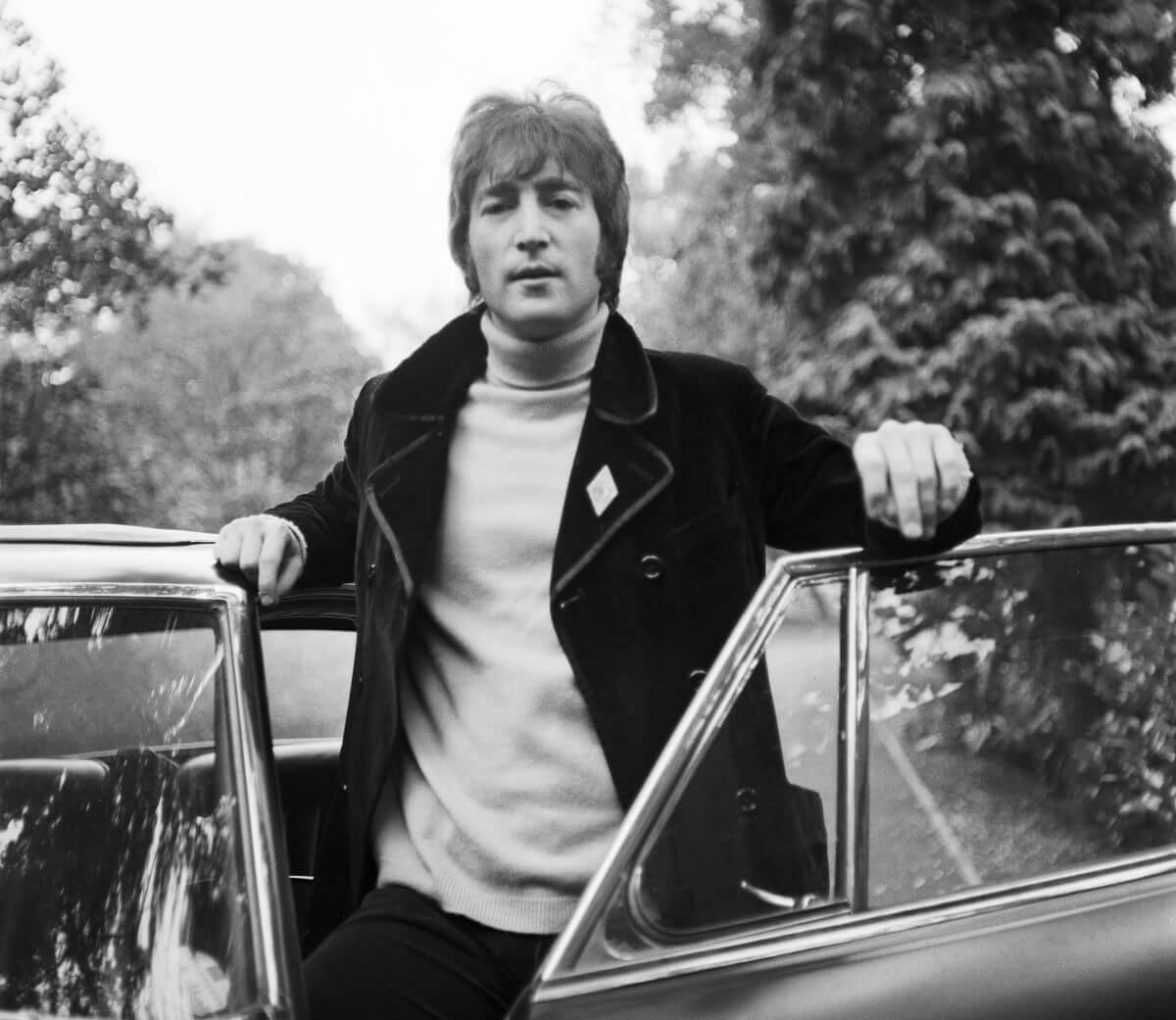 A black and white picture of John Lennon standing in an open car door.
