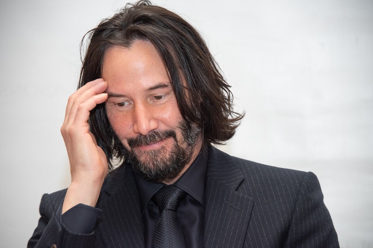 Keanu Reeves in a black suit holding his head at the 'John Wick Chapter 3' press conference.