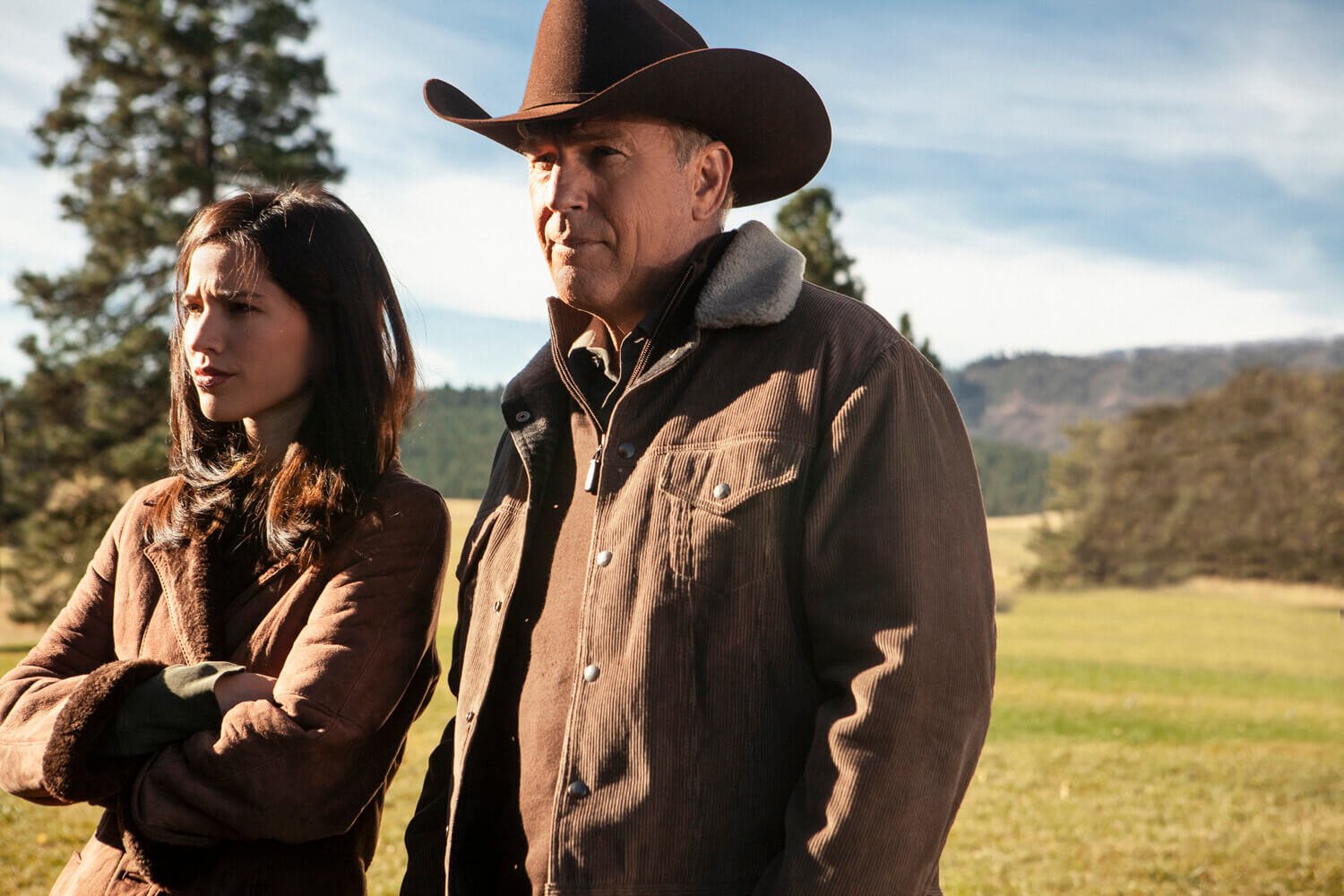 Kelsey Asbille as Monica Dutton and Kevin Costner as John Dutton standing side by side in 'Yellowstone'