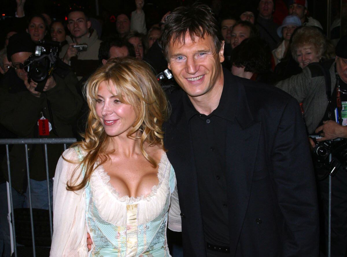 Natasha Richardson wears a white dress and stands with Liam Neeson, who wears a black shirt.