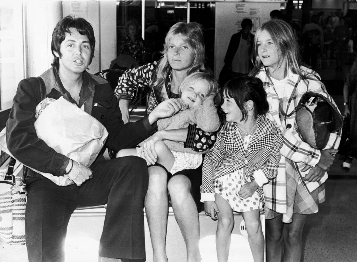 A black and white picture of Paul McCartney sitting with his family, Linda, Stella, Mary, and Heather.
