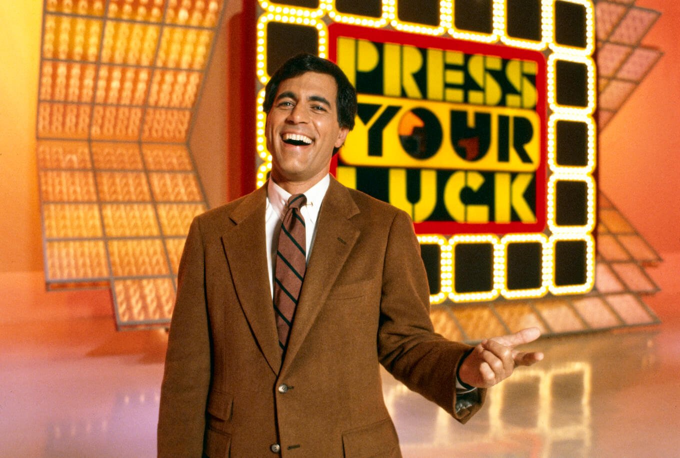 'Press Your Luck' host Peter Tomarken laughing in front of the game show's sign