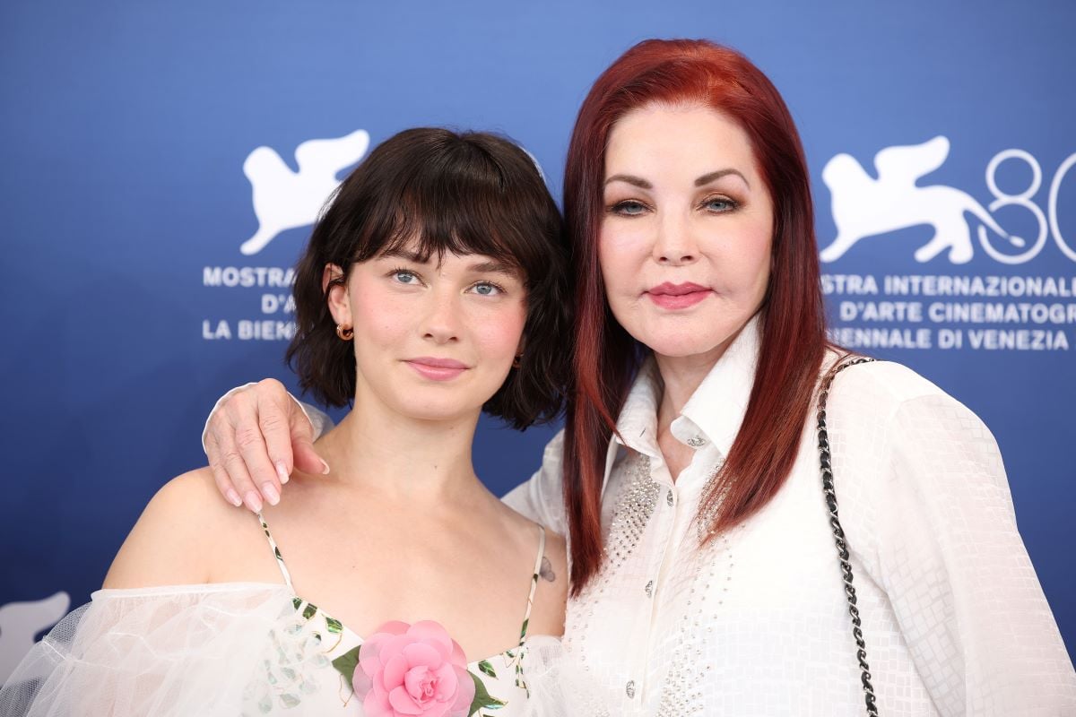 Priscilla Presley stands with her arm around Cailee Spaeny's shoulders. They both wear white.