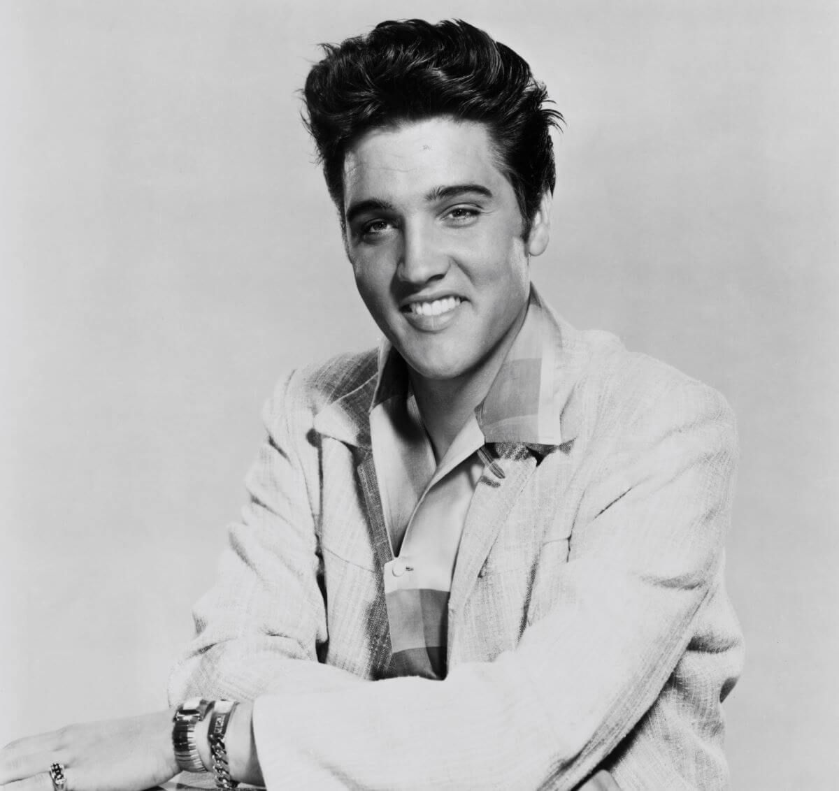 A black and white picture of Elvis Presley sitting with his arms resting on his guitar.