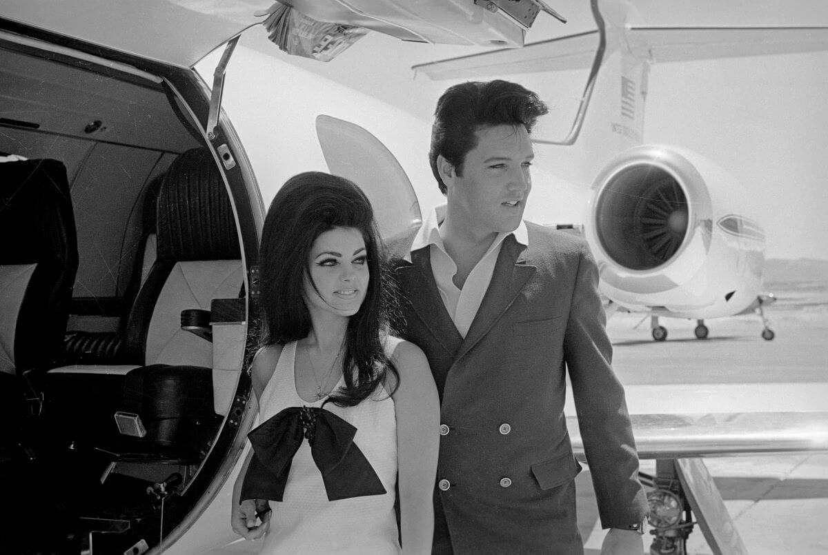 Priscilla and Elvis Presley stand in the open door of an airplane.