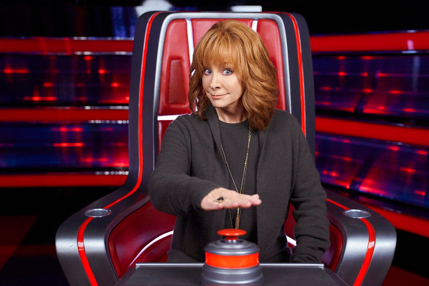 Reba McEntire in 'The Voice' looking mischievous as she holds her hand over the red button