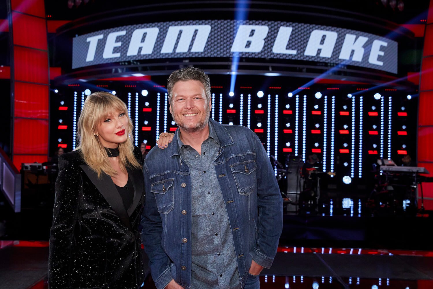 Taylor Swift and Blake Shelton with a 'Team Blake' banner behind them in 'The Voice'