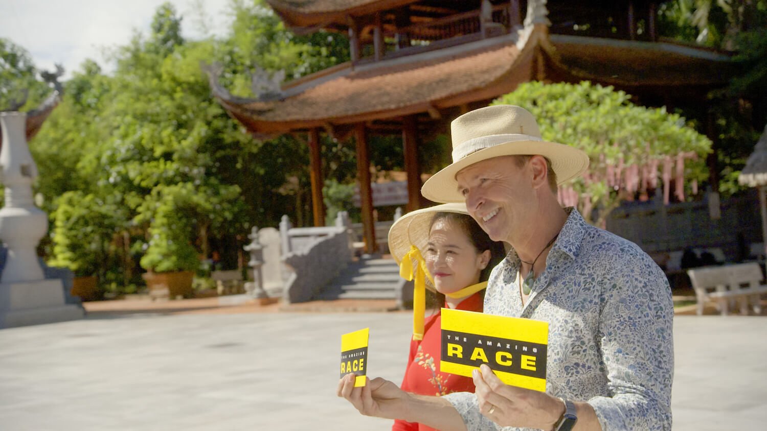 Phil Keoghan at a finish line holding a card in 'the Amazing Race' Season 35