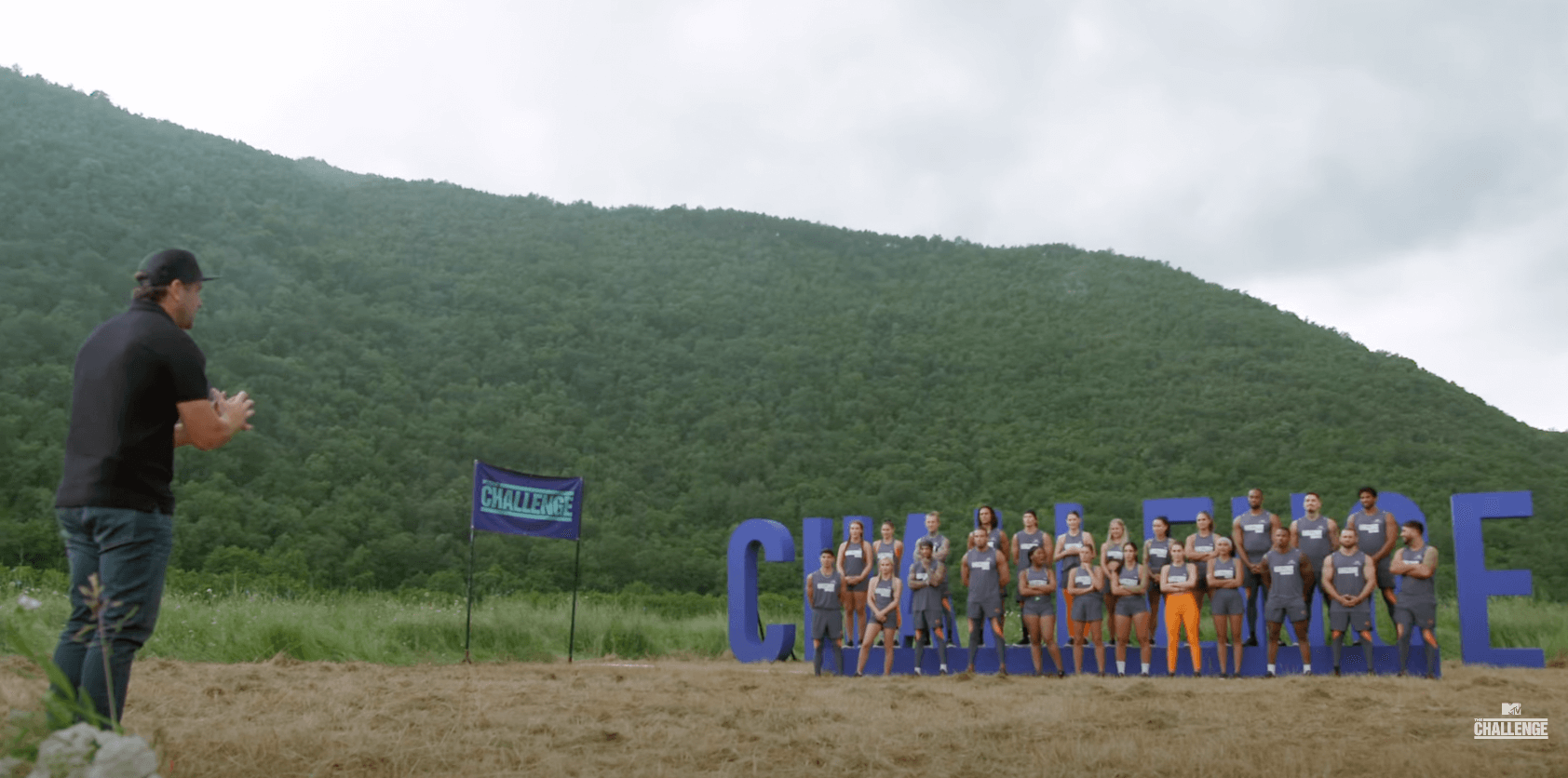 T.J. Lavin talking to 'The Challenge' Season 39 cast about the format and twists of the season while they stand in front of 'The Challenge' sign