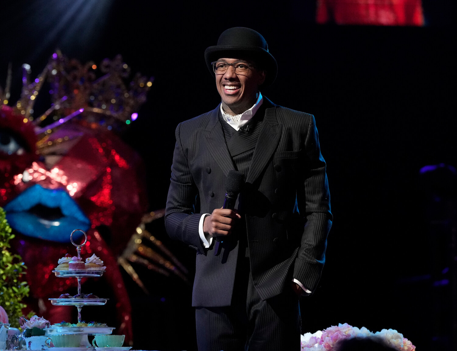 Nick Cannon, the host of 'The Masked Singer' Season 10, wearing all black on stage
