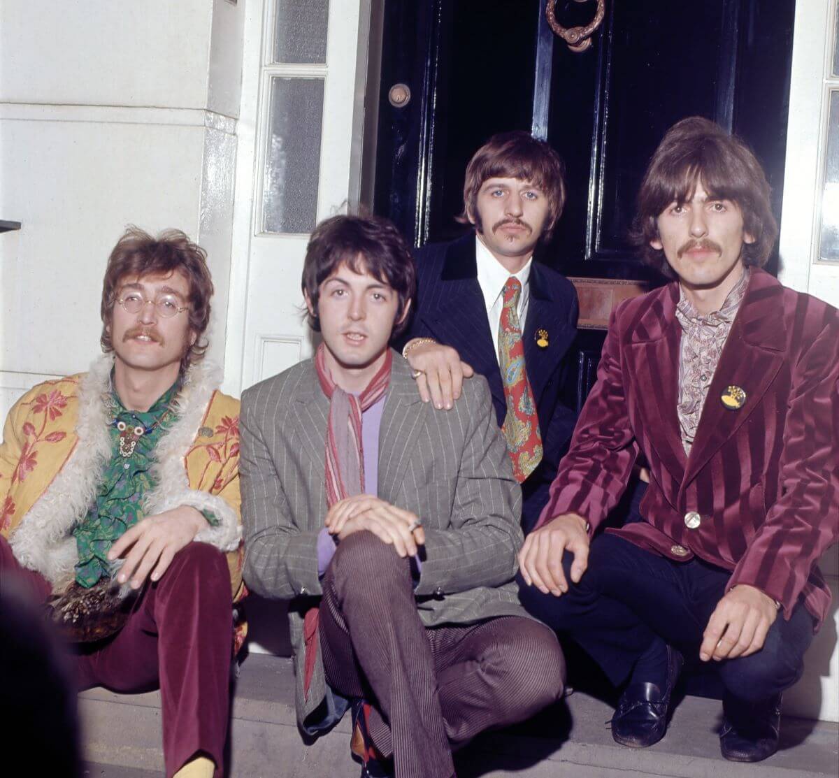 John Lennon, Paul McCartney, Ringo Starr, and George Harrison of The Beatles crouch on a doorstep.
