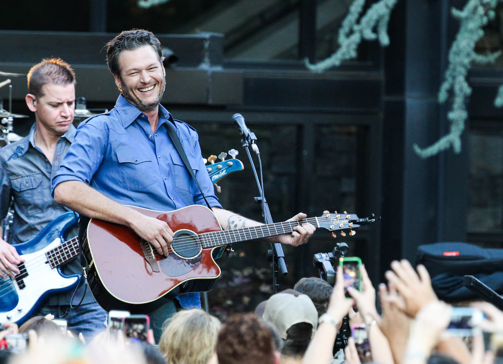 Blake Shelton holding a guitar in front of a crowd and smiling