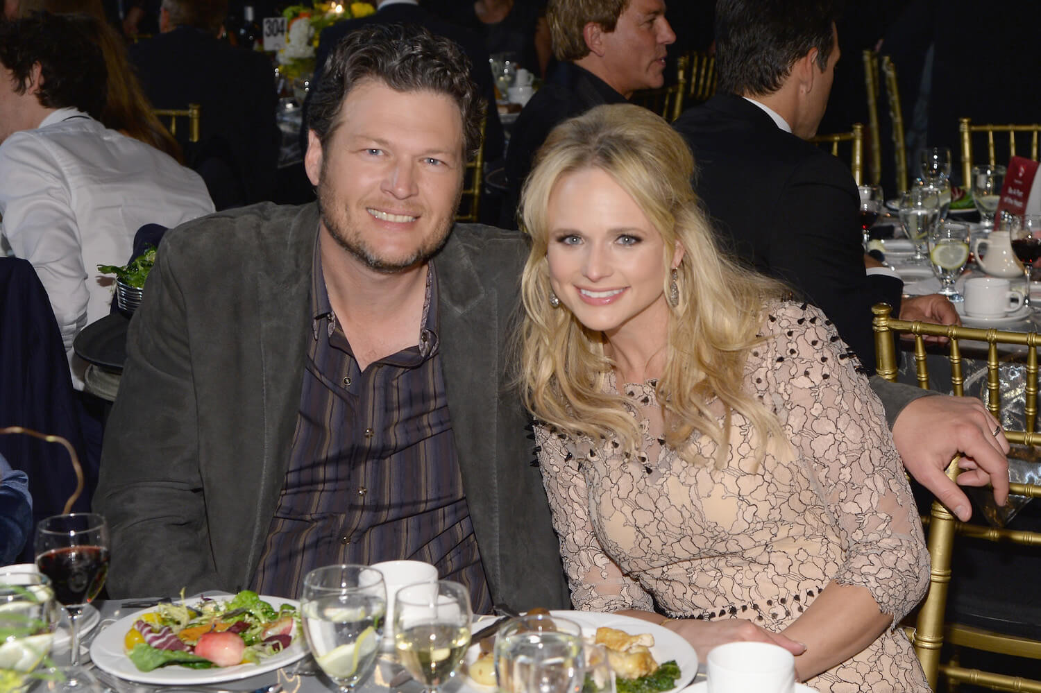 Blake Shelton with his arm around Miranda Lambert in 2014. They're smiling with dinner in front of them at a table