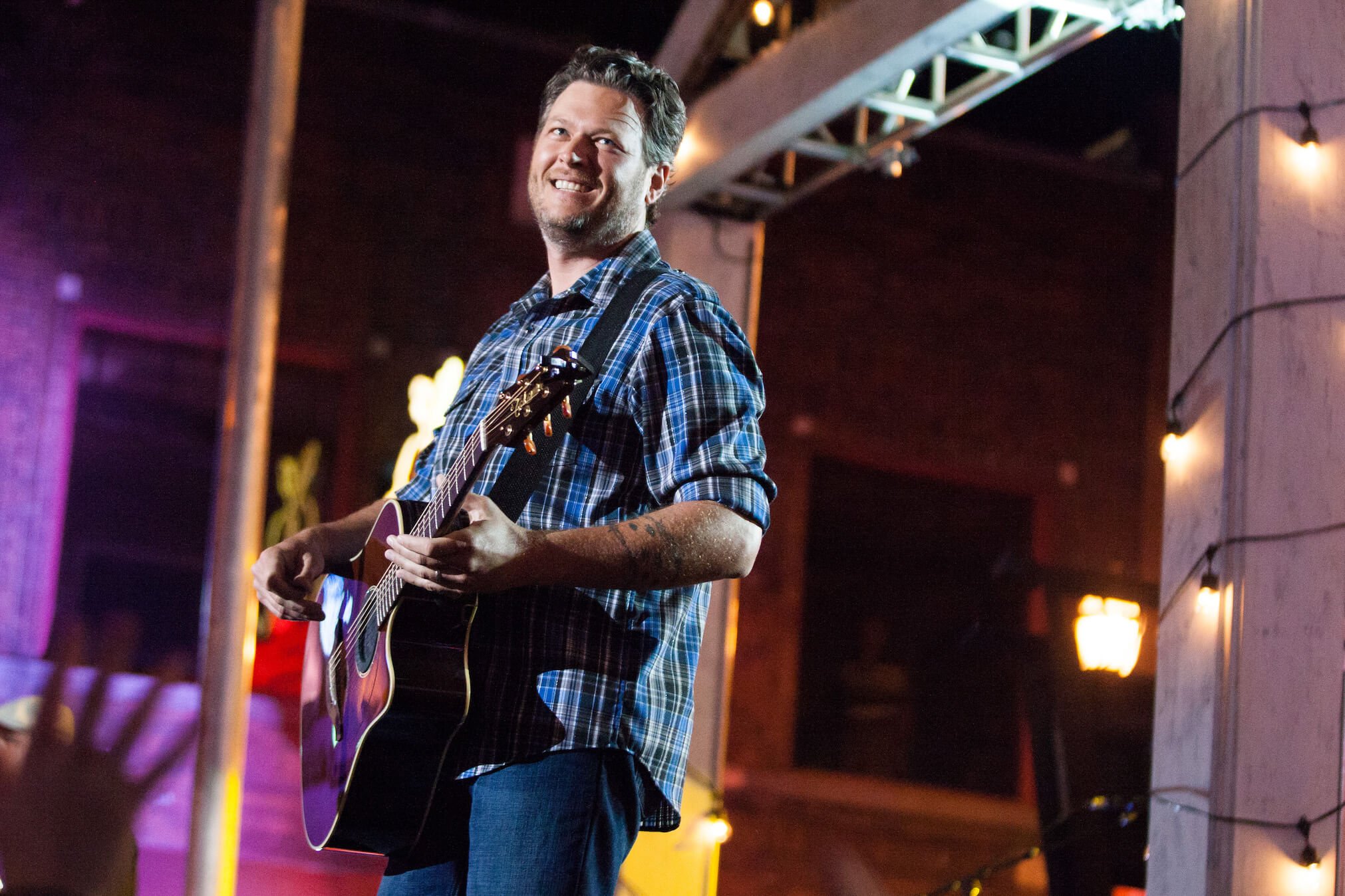 Blake Shelton holding a guitar and smiling during a concert