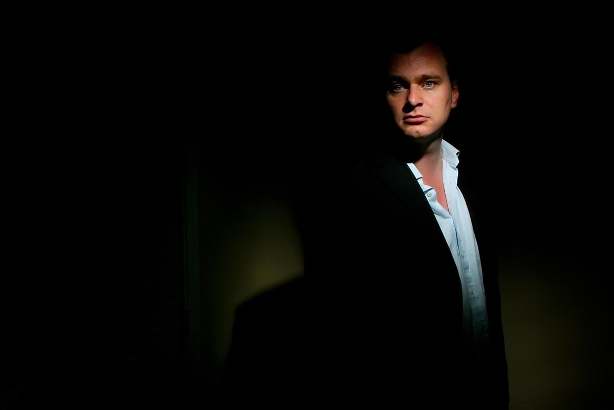 Christopher Nolan posing in a dark room wearing a suit.