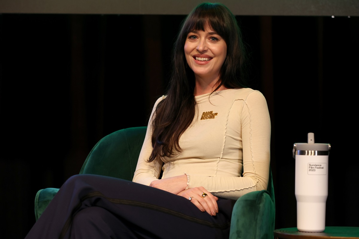 Dakota Johnson speaking at the 2023 Sundance Film Festival Women at Sundance Celebration while wearing a tan shirt and black pants.