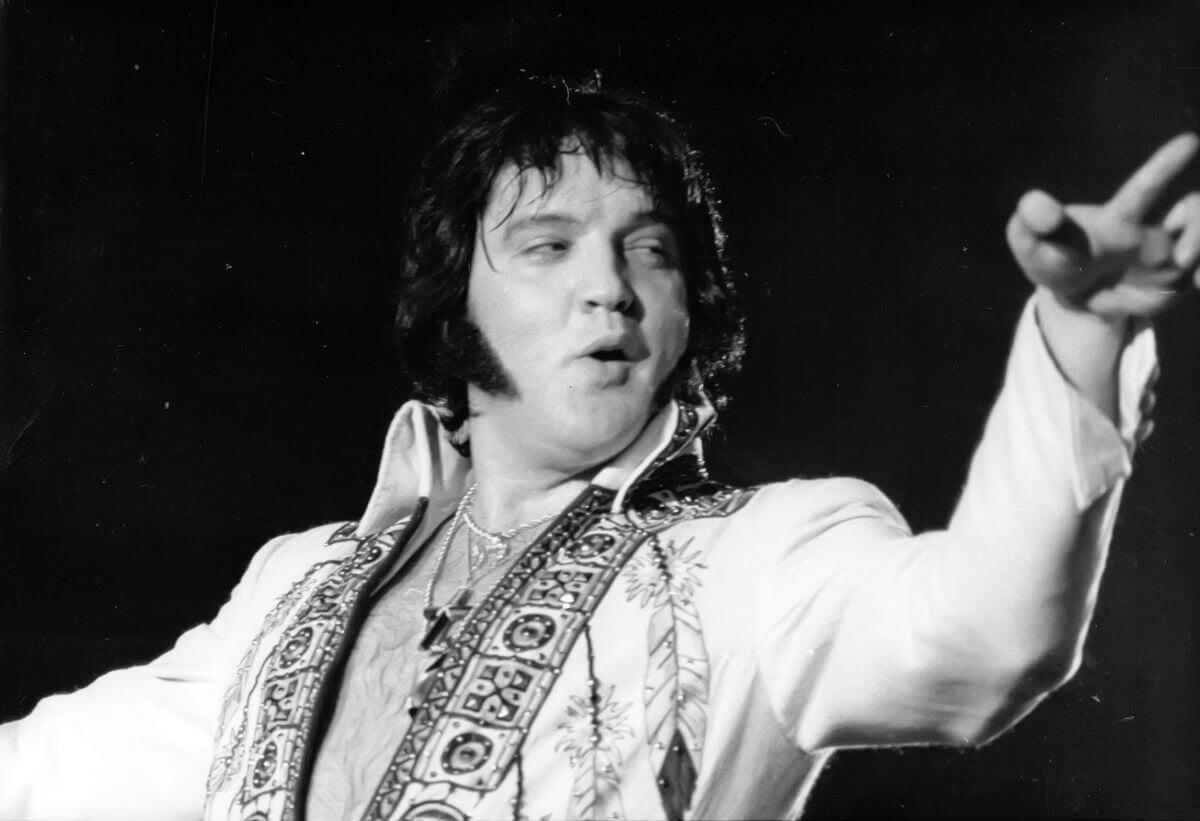 A black and white picture of Elvis wearing an unzipped jumpsuit.