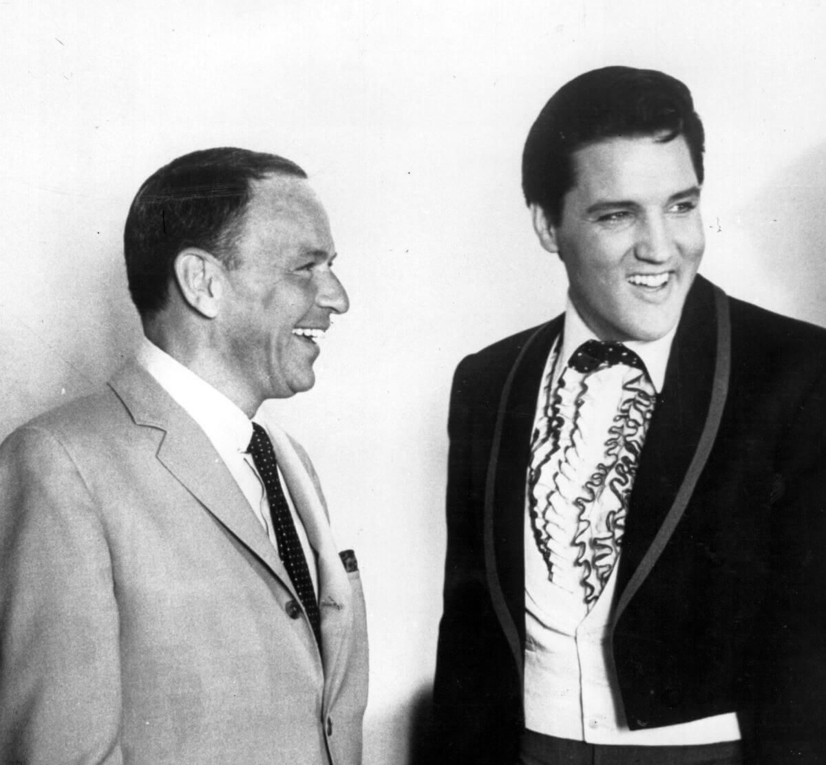A black and white picture of Frank Sinatra and Elvis standing together. They both wear suits.