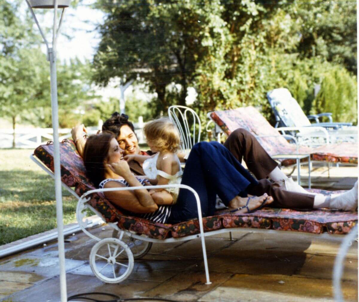 Priscilla and Elvis Presley lay on lounge chairs. Lisa Marie Presley sits on Priscilla's stomach.