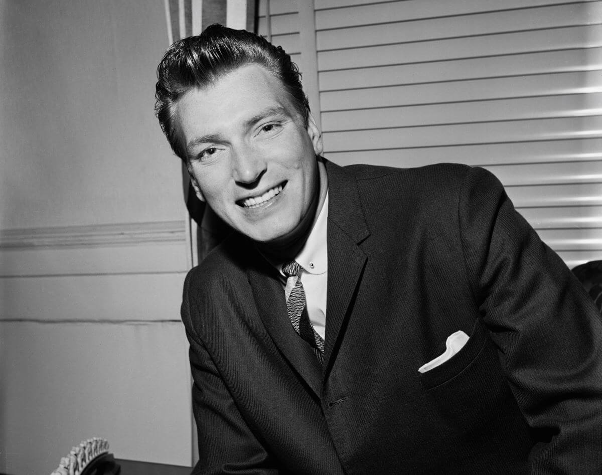 A black and white picture of Frank Ifield wearing a suit and sitting in front of a window.