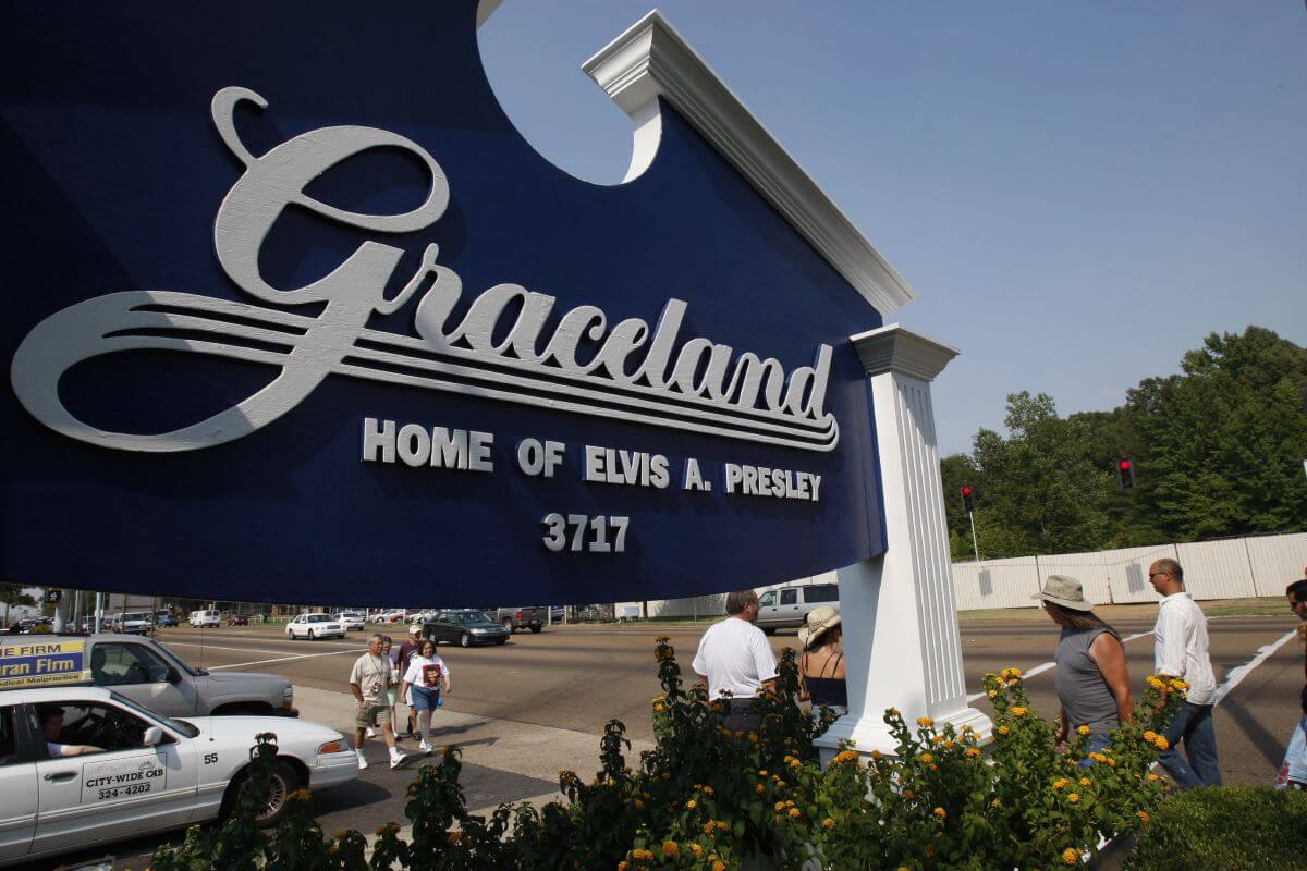 A blue sign that reads "Graceland: Home of Elvis A. Presley." Several people walk behind it.