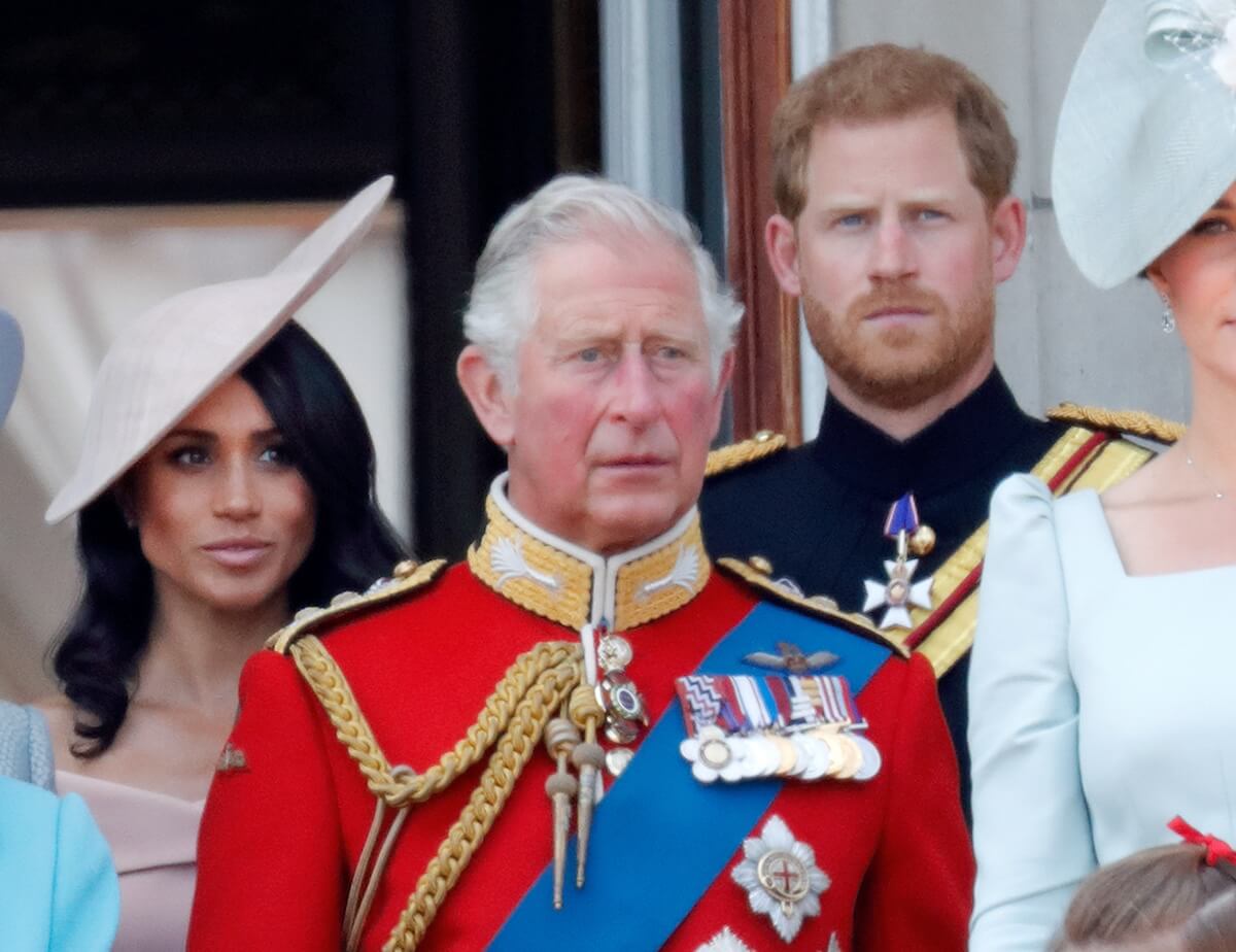 Meghan Markle and Prince Harry stand behind King Charles