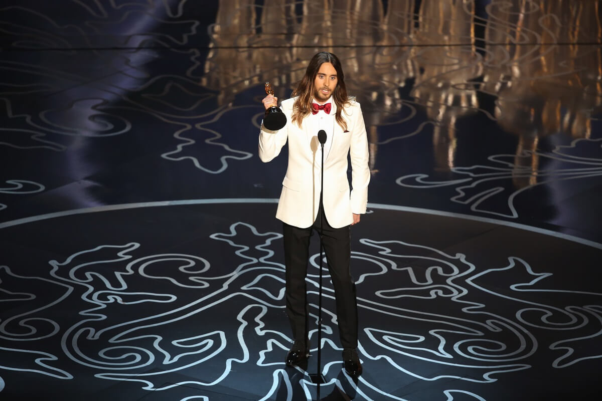 Jared Leto holding an Oscar award on stage while wearing a suit.