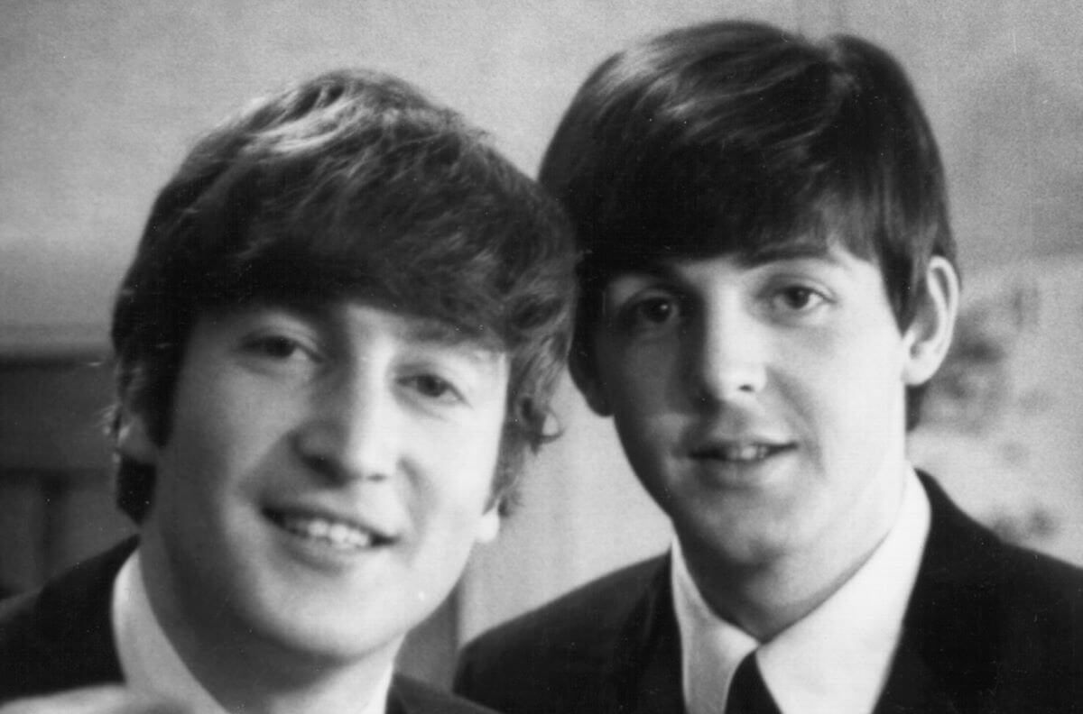 A black and white picture of John Lennon and Paul McCartney wearing suits and smiling at the camera.