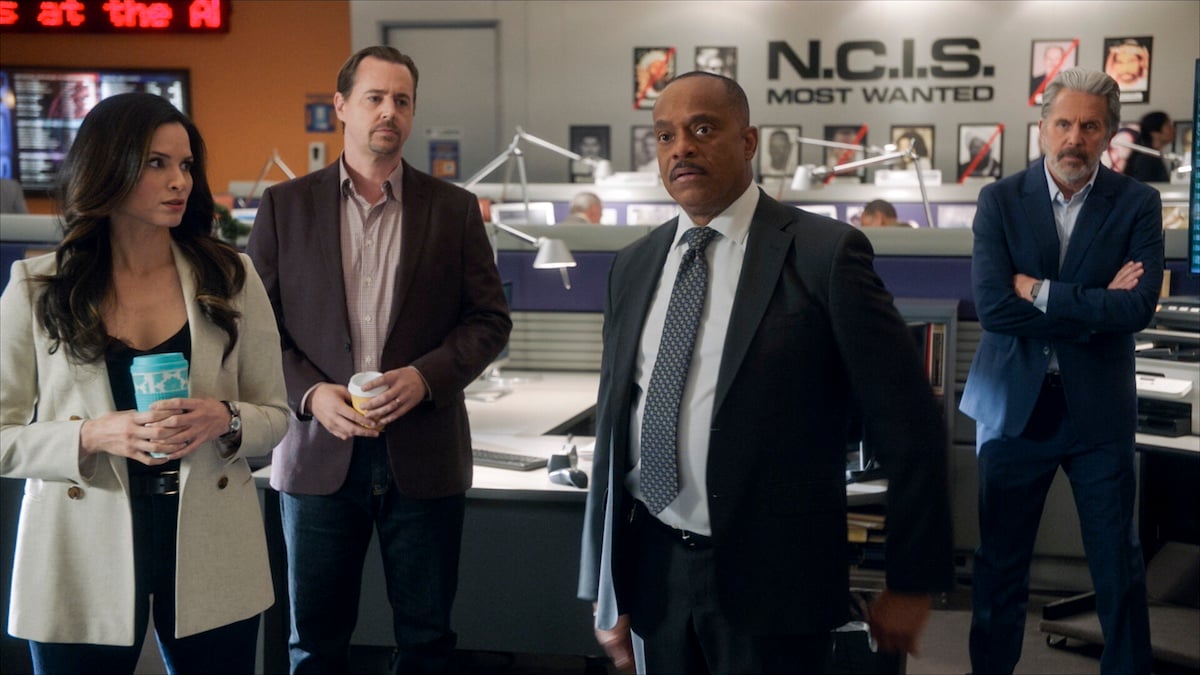 NCIS agents standing in an office with the NCIS logo behind them