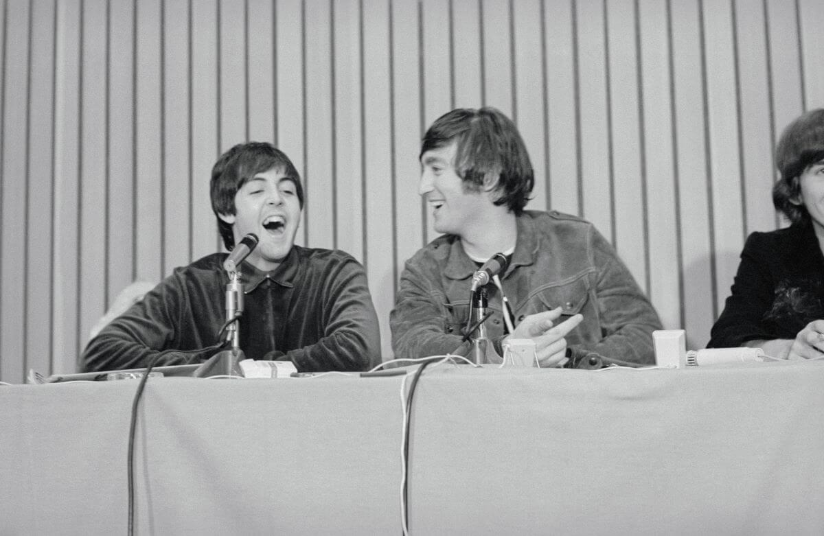 A black and white picture of Paul McCartney and John Lennon sitting behind microphones and laughing.