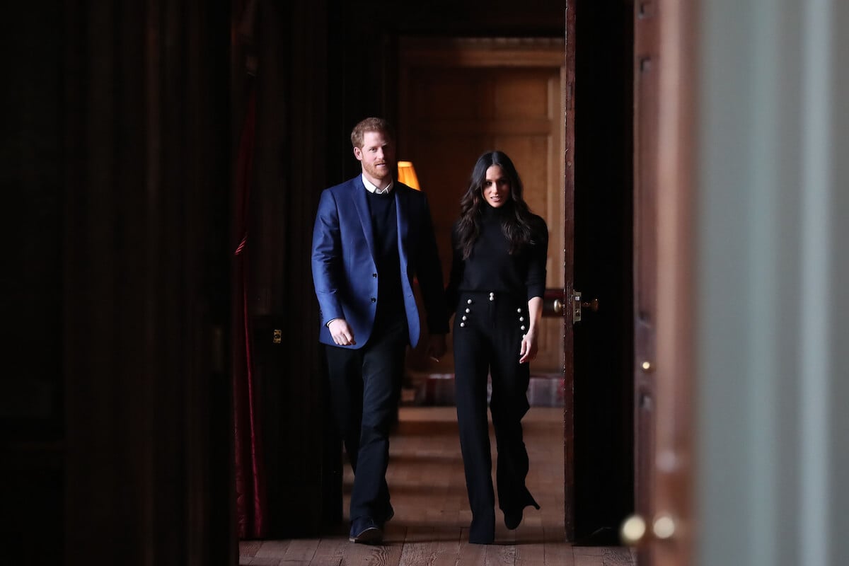 Prince Harry and Meghan Markle, who may spend New Year's with King Charles, walk down a hallway
